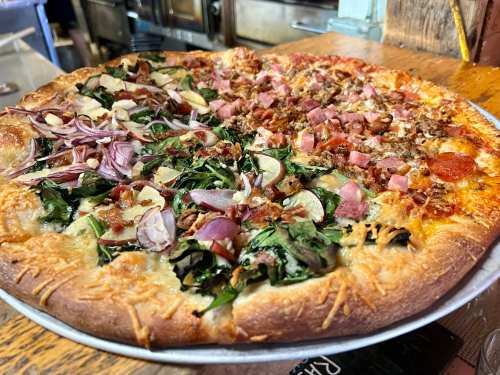 A large pizza with two halves: one topped with greens, bacon, and onions, the other with pepperoni and cheese.