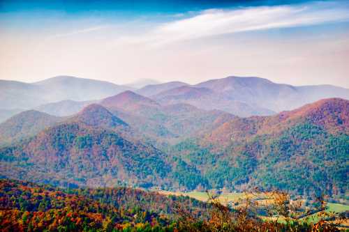 A scenic view of rolling mountains with autumn foliage under a blue sky and soft clouds.