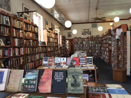 A cozy bookstore filled with shelves of books, featuring a central table displaying various titles.