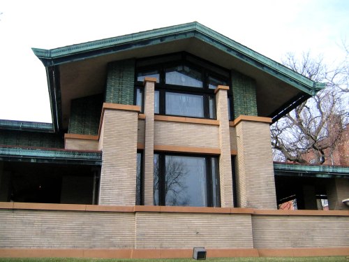 A modern architectural building with a distinctive roof, large windows, and a mix of brick and green accents.