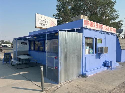 A blue food stand with a sign reading "All Points Grill," serving burgers, shakes, fries, and hot dogs. Outdoor seating visible.