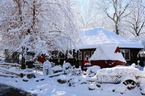 A cozy house covered in snow, surrounded by snow-laden trees and a winter landscape.