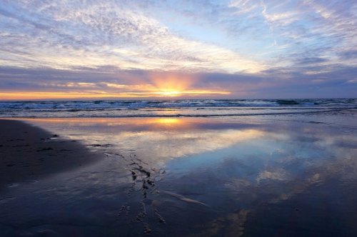 A serene beach at sunset, with vibrant colors reflecting on the wet sand and gentle waves lapping at the shore.