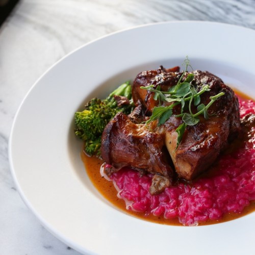 A plate featuring roasted meat on vibrant pink risotto, garnished with greens and accompanied by broccoli.