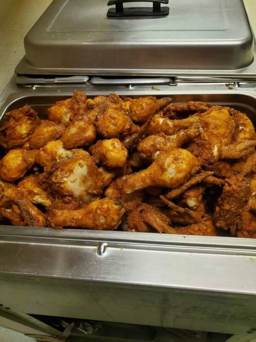 A metal tray filled with golden-brown fried chicken pieces, including drumsticks and wings.