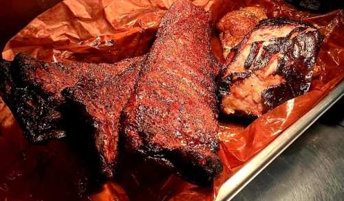 A platter of smoked meats, including ribs and a brisket, resting on brown parchment paper.