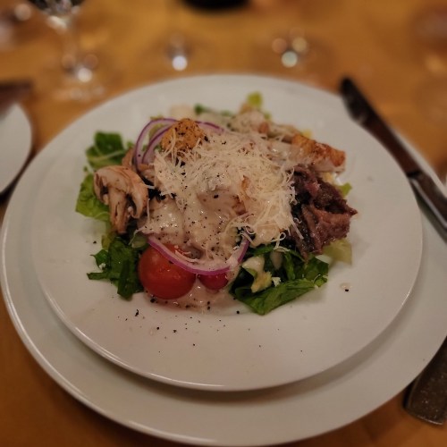 A fresh salad with greens, cherry tomatoes, grilled chicken, red onions, and grated cheese on a white plate.