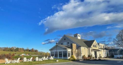 A modern building with a stone facade, surrounded by white chairs, under a blue sky with fluffy clouds.