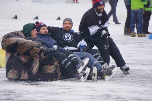 Four men in hockey skates sit on a couch on an ice rink, enjoying a casual moment together.