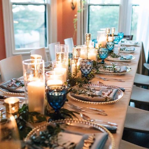 A beautifully set dining table with candles, decorative glassware, and greenery, ready for a gathering.
