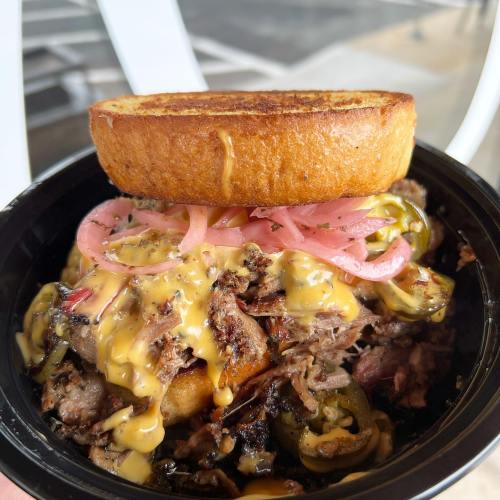 A bowl filled with shredded meat, jalapeños, pickled onions, and melted cheese, topped with a toasted bread slice.