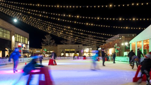 A lively outdoor ice skating rink at night, adorned with string lights and colorful decorations, with skaters in motion.