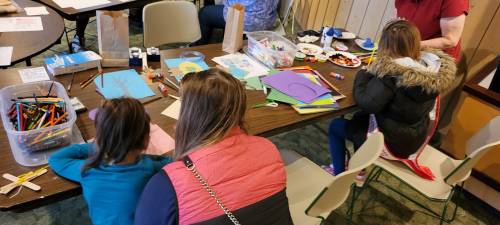 Two children and an adult engage in arts and crafts at a table filled with supplies and colorful materials.
