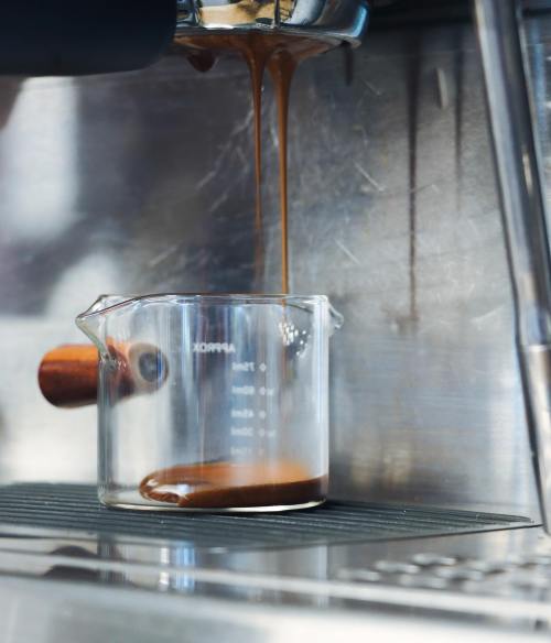 A close-up of espresso pouring from a machine into a measuring cup on a stainless steel surface.