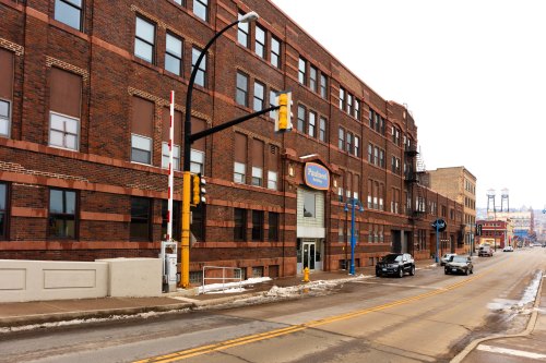 A brick building with a sign, alongside a snowy street with parked cars and traffic lights.