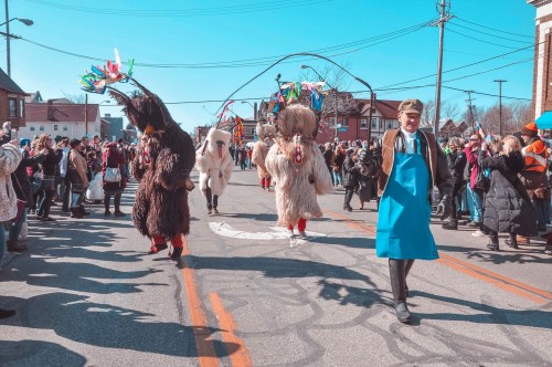 Colorful parade with costumed figures and a crowd watching on a sunny day, featuring traditional attire and festive decorations.