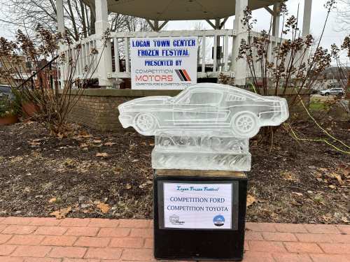 Ice sculpture of a car at the Logan Town Center Frozen Festival, with a sign for Competition Motors in the background.
