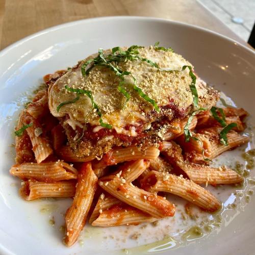 A plate of pasta topped with a breaded chicken cutlet, marinara sauce, cheese, and fresh basil.