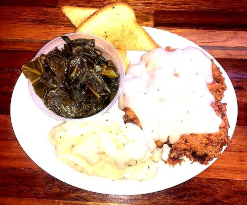 A plate of fried chicken with gravy, mashed potatoes, collard greens, and a slice of toast.