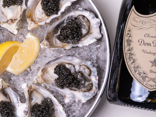 A platter of oysters topped with caviar, accompanied by lemon wedges and a bottle of Dom Pérignon champagne.