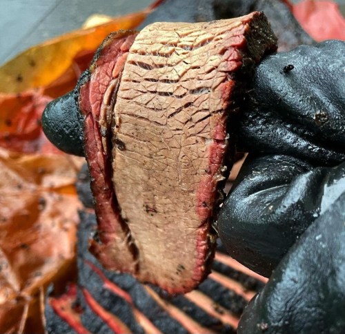 Close-up of a hand holding a slice of smoked brisket, showcasing its juicy texture and smoky flavor.