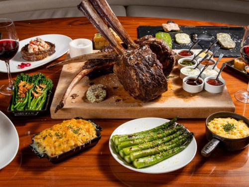 A lavish dining spread featuring a large ribeye steak, asparagus, macaroni and cheese, and various sauces.
