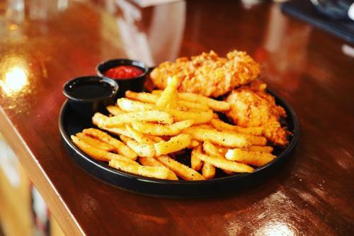 A plate of crispy fried chicken with golden French fries and two dipping sauces on a wooden table.