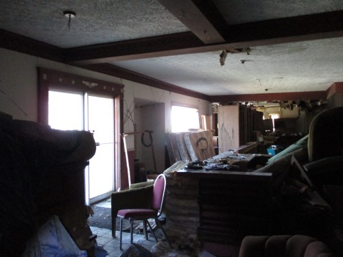 An abandoned room filled with debris, furniture, and dim lighting, showing signs of neglect and disrepair.