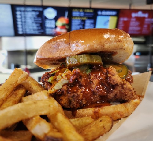A close-up of a crispy fried chicken sandwich with pickles, served with a side of golden French fries.