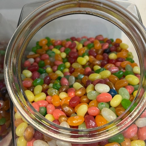 A clear jar filled with colorful jelly beans in various shades of red, green, yellow, and orange.