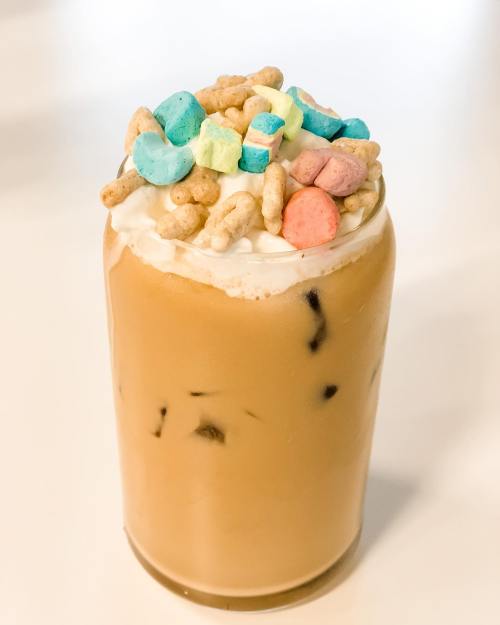 A tall glass of iced coffee topped with whipped cream and colorful cereal pieces.