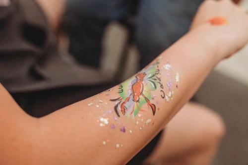 A close-up of a colorful crab tattoo on a person's arm, adorned with glitter and floral designs.