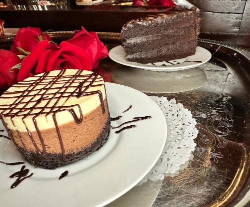 A chocolate mousse cake and a slice on a silver tray, surrounded by red roses and a lace doily.