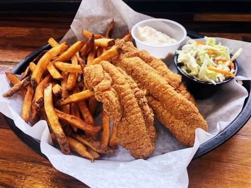 A plate of crispy fried fish fillets with golden fries and a side of coleslaw and dipping sauce.