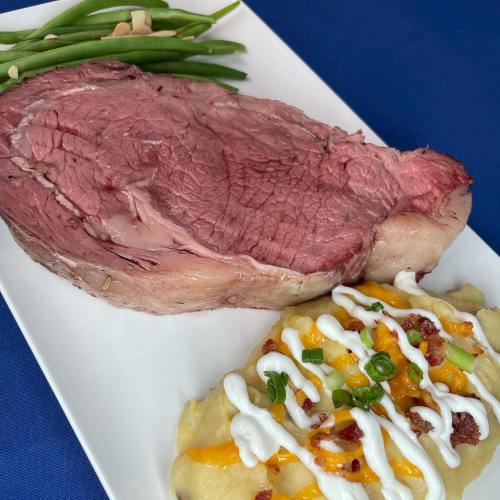A plate featuring a juicy slice of prime rib, creamy loaded mashed potatoes, and green beans with almonds.