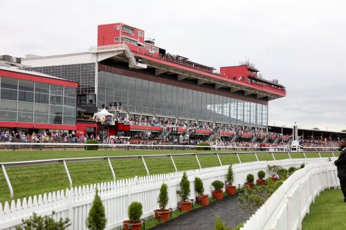 A large crowd gathers at a racetrack with a modern grandstand and green grass in the foreground.