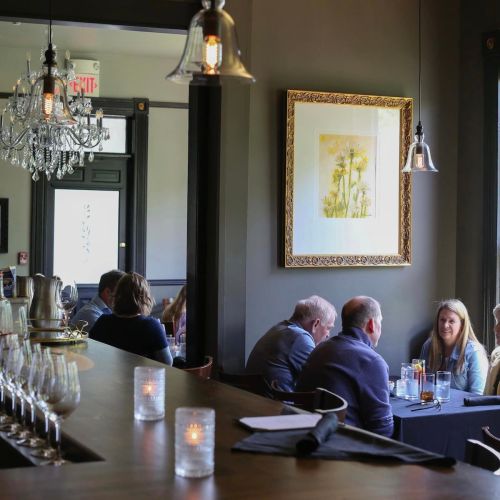A cozy restaurant interior with diners at tables, elegant lighting, and a floral artwork on the wall.
