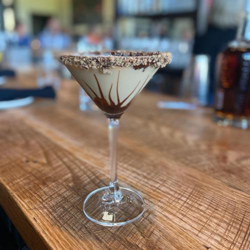A dessert martini with a chocolate rim, served in a clear glass on a wooden table.