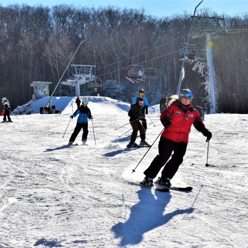 Skiers navigate a snowy slope with ski lifts in the background on a bright, sunny day.