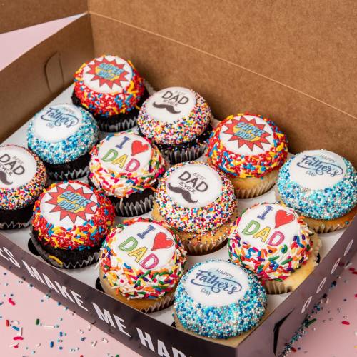 A box of colorful cupcakes decorated for Father's Day with various designs and sprinkles.