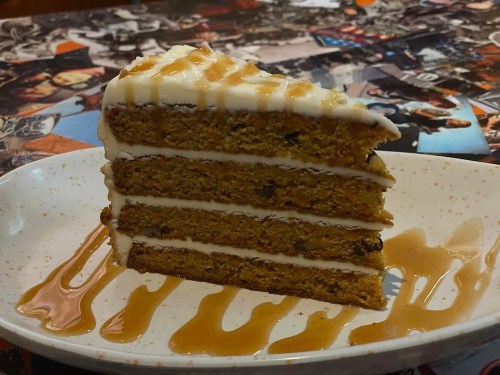 A slice of layered cake with cream frosting and caramel drizzle on a decorative plate.