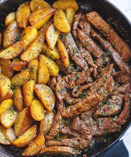 A skillet filled with golden roasted potatoes and savory strips of beef, garnished with herbs.