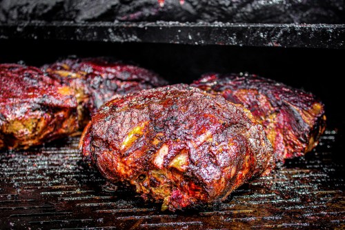Three smoked meat cuts with a dark, charred exterior resting on a grill.