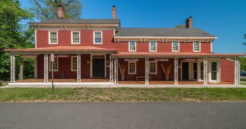 A red two-story house with white trim, featuring a porch and multiple windows, set against a clear blue sky.