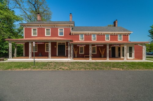 A large red two-story house with white trim and a porch, set against a clear blue sky and green trees.