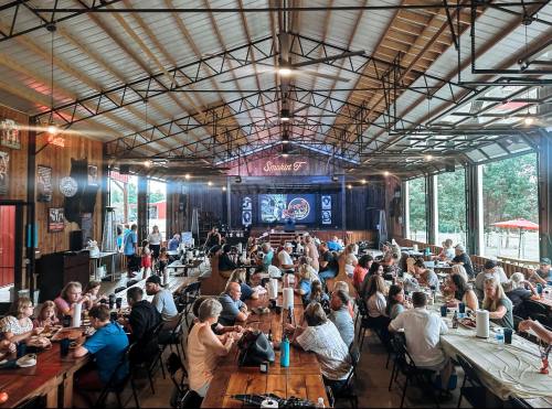 A lively indoor dining space filled with people enjoying a meal at long tables, with a stage in the background.