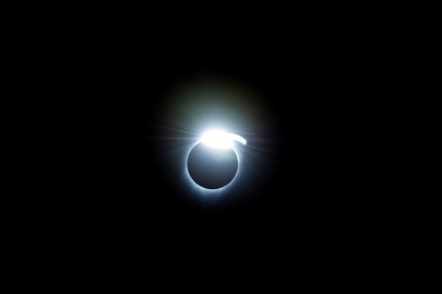 A bright light encircles a dark sphere, resembling a solar eclipse against a black background.