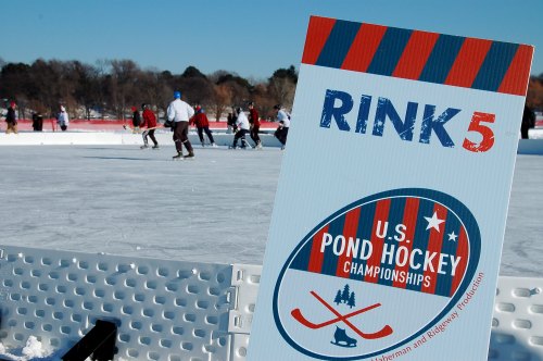 Sign for Rink 5 at the U.S. Pond Hockey Championships, with players skating on an ice rink in the background.