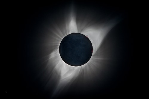 A solar eclipse with a darkened sun surrounded by glowing corona and rays of light extending outward.