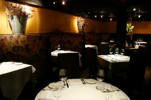 Elegant restaurant interior with neatly set tables, soft lighting, and floral decor on the walls.